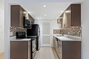 Kitchen featuring appliances with stainless steel finishes, dark brown cabinets, light stone counters, recessed lighting, and tasteful backsplash