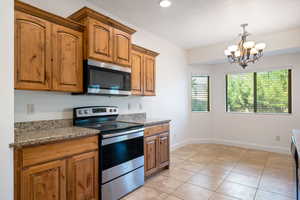 Kitchen featuring stainless steel appliances, light stone counters, hanging light fixtures, brown cabinetry, and a chandelier