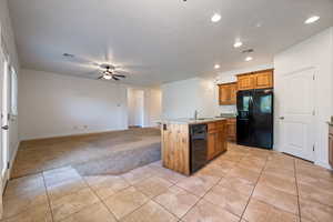 Kitchen featuring light colored carpet, black appliances, brown cabinets, light stone countertops, and open floor plan