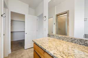 Bathroom featuring a shower stall, a walk in closet, vanity, light tile patterned floors, and light colored carpet