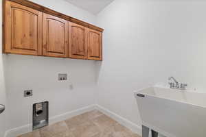 Laundry area with hookup for a washing machine, electric dryer hookup, cabinet space, and light tile patterned flooring