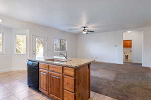 Kitchen featuring brown cabinets, arched walkways, a kitchen island with sink, light stone countertops, and open floor plan