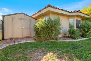 View of side of home featuring a shed, a lawn, a tiled roof, and stucco siding