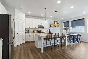 Kitchen with stainless steel appliances, pendant lighting, a kitchen island with sink, a kitchen breakfast bar, and open shelves