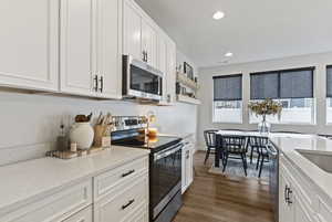Kitchen featuring stainless steel appliances, white cabinetry, light stone countertops, dark wood-type flooring, and recessed lighting