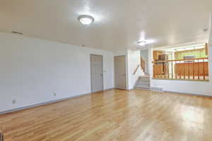 Unfurnished living room with a textured ceiling, stairway, and light wood finished floors