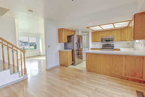 Kitchen with light countertops, a peninsula, appliances with stainless steel finishes, light wood-type flooring, and a textured ceiling