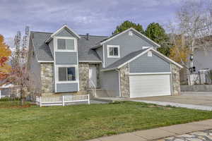 View of front of house with stone siding, concrete driveway, roof with shingles, and an attached garage