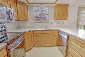 Kitchen featuring stainless steel appliances, light floors, light countertops, light brown cabinetry, and a peninsula