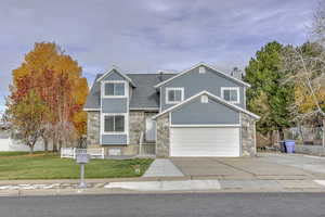 View of front of property with stone siding, driveway, a chimney, and a garage
