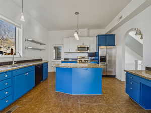 Kitchen with blue cabinets, open shelves, dark stone counters, stainless steel appliances, and pendant lighting