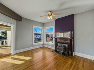 Unfurnished living room featuring wood finished floors, a ceiling fan, and a fireplace with flush hearth