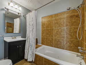 Full bath with a combined bath / shower with jetted tub, vanity, and a textured ceiling