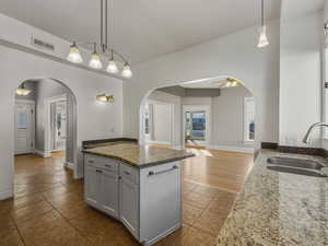 Kitchen featuring dark stone counters, decorative light fixtures, arched walkways, light tile patterned floors, and open floor plan