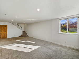 Unfurnished living room featuring carpet, a textured ceiling, recessed lighting, and stairway