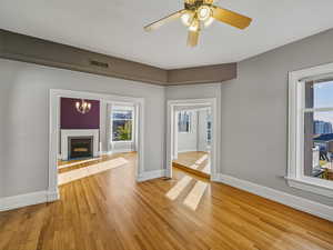 Unfurnished living room featuring light wood-style flooring, a fireplace with raised hearth, a ceiling fan, and a chandelier
