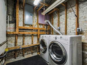 Laundry area featuring brick wall, electric panel, and washing machine and dryer