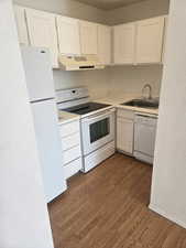 Kitchen featuring white appliances, white cabinetry, light countertops, range hood, and a textured wall