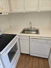 Kitchen with white appliances, white cabinetry, light countertops, dark wood-type flooring, and under cabinet range hood