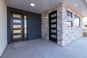 Property entrance featuring stone siding, stucco siding, and a patio