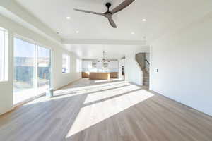 Unfurnished living room featuring light wood-type flooring, a ceiling fan, a chandelier, recessed lighting, and stairs