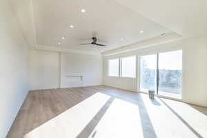 Unfurnished living room featuring light wood-style floors, a raised ceiling, a ceiling fan, and recessed lighting