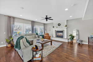 Living room with a high end fireplace, dark wood-type flooring, recessed lighting, arched walkways, and ceiling fan