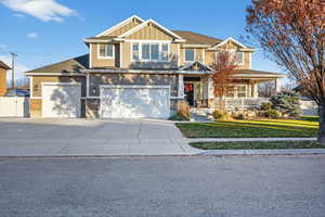 Craftsman-style house with stone siding, covered porch, board and batten siding, a front yard, and driveway