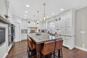 Kitchen with glass insert cabinets, white cabinetry, light stone countertops, and recessed lighting