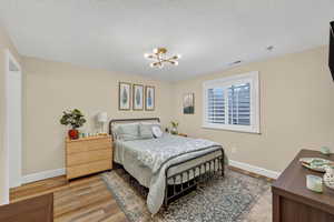 Bedroom with a textured ceiling, light wood-style flooring, and a chandelier