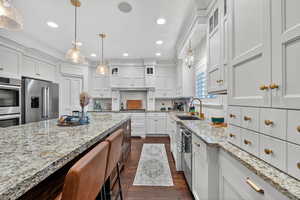 Kitchen with glass insert cabinets, white cabinetry, stainless steel appliances, light stone countertops, and recessed lighting