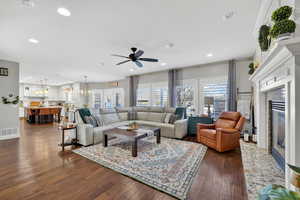 Living room with ceiling fan, a fireplace, dark wood-type flooring, recessed lighting, and a chandelier