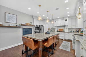 Kitchen with light stone counters, white cabinets, decorative backsplash, stainless steel appliances, and dark wood-style floors