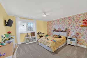 Carpeted bedroom featuring wallpapered walls, crown molding, and a ceiling fan