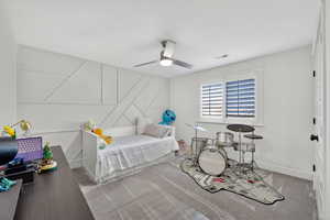 Carpeted bedroom with a ceiling fan and a decorative wall