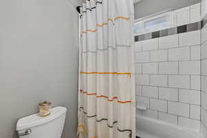 Full bathroom featuring shower / bathtub combination with curtain and toilet