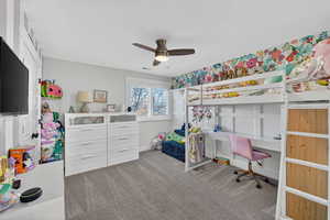 Bedroom featuring light colored carpet, ceiling fan, and a desk
