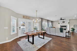 Dining room featuring dark wood-type flooring, a chandelier, arched walkways, and a warm lit fireplace