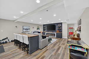 Living room featuring light wood-type flooring, recessed lighting, a glass covered fireplace, and beamed ceiling