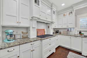 Kitchen featuring glass insert cabinets, backsplash, white cabinetry, light stone counters, and dark wood finished floors