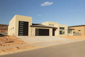 Contemporary house featuring stucco siding, a garage, driveway, and stone siding