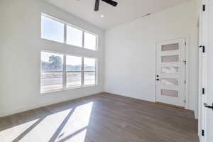 Unfurnished room with dark wood-style flooring, a ceiling fan, and a high ceiling