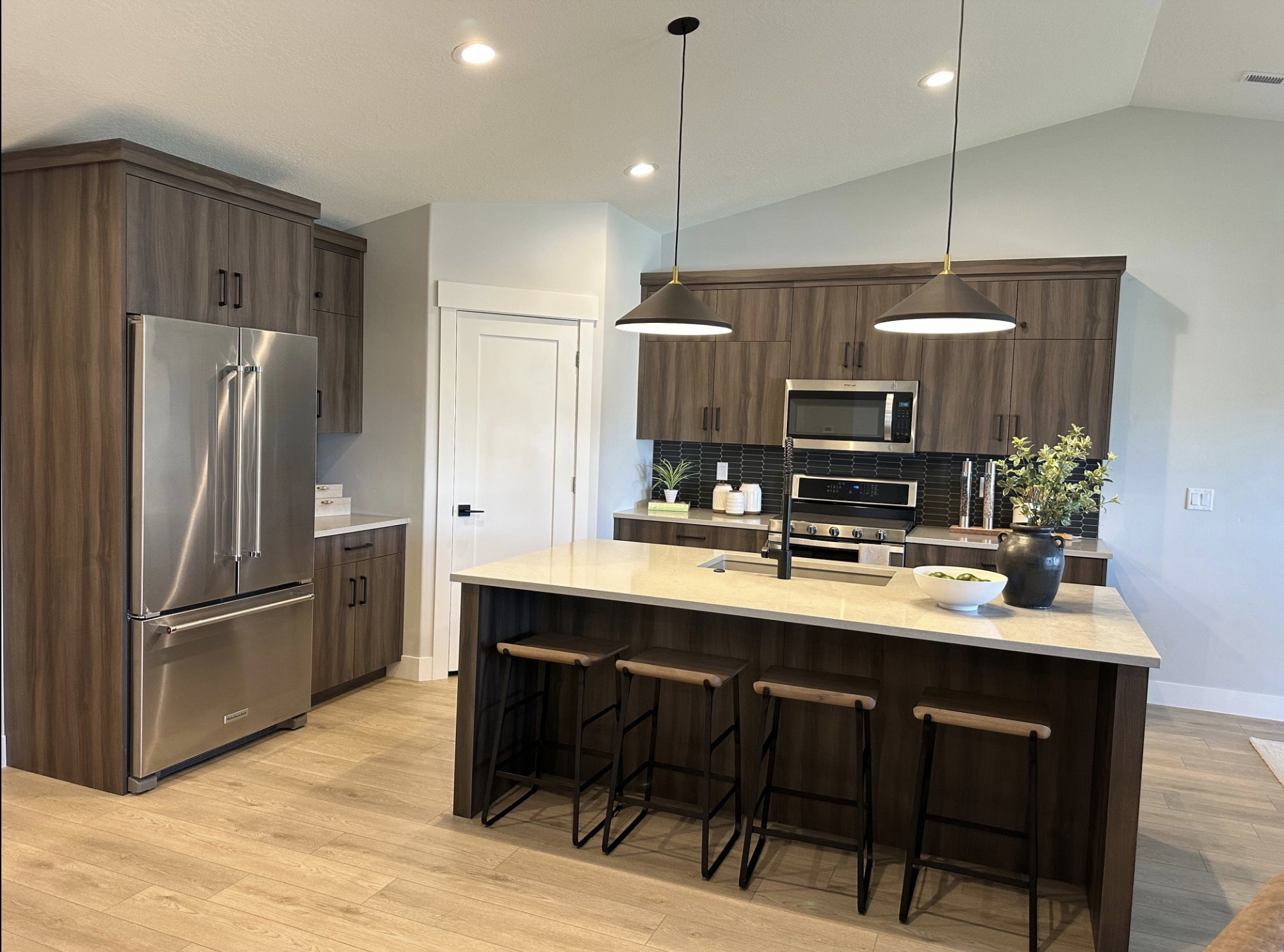 Kitchen with stainless steel appliances, a kitchen bar, dark brown cabinets, decorative light fixtures, and vaulted ceiling