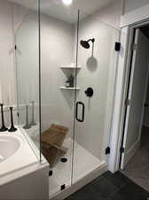 Bathroom featuring a marble finish shower, vanity, and dark tile patterned floors
