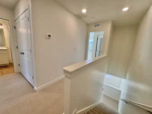 Hall with an upstairs landing, light colored carpet, and recessed lighting