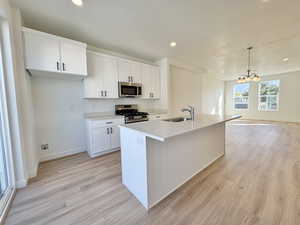 Kitchen featuring white cabinets, appliances with stainless steel finishes, a center island with sink, hanging light fixtures, and recessed lighting