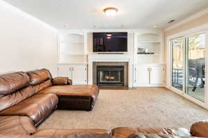 Carpeted living area featuring built in features, a fireplace, crown molding, and a textured ceiling