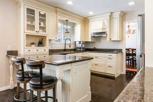 Kitchen featuring dark stone countertops, pendant lighting, a breakfast bar, recessed lighting, and glass insert cabinets