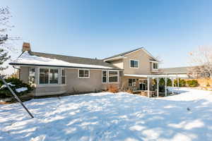 Snow covered property with a patio area, stucco siding, a chimney, and roof with shingles