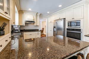 Kitchen featuring a peninsula, appliances with stainless steel finishes, dark stone countertops, a kitchen bar, and recessed lighting